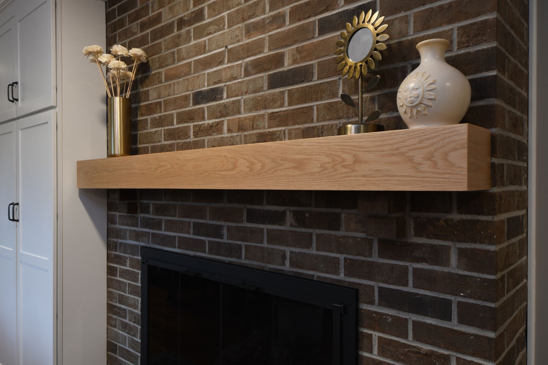 Brick fireplace with a wooden mantel, decorative vase, and flowers against a brick wall.