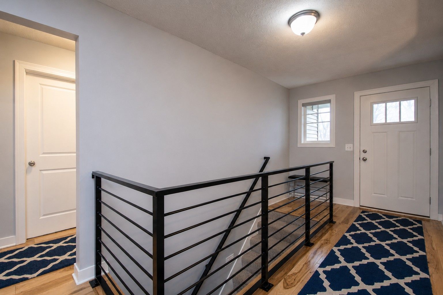 Bright entryway with black stair railing, white doors, and blue patterned runners on the floor.