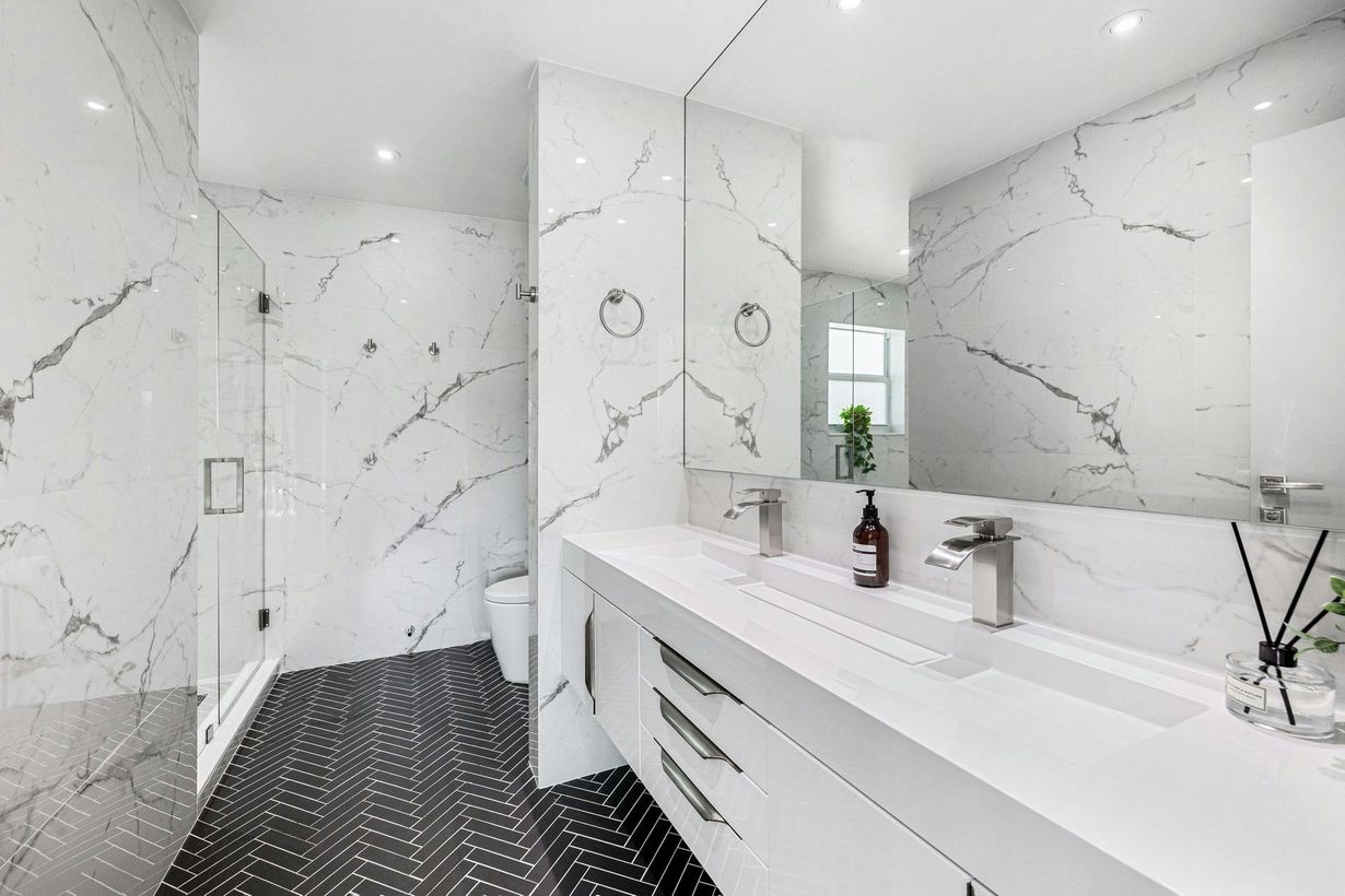 Modern white bathroom with marble walls, black hex tile floor, and a long vanity with sink.