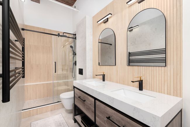 Modern bathroom with glass shower, floating vanity, twin arched mirrors, and wood slat walls