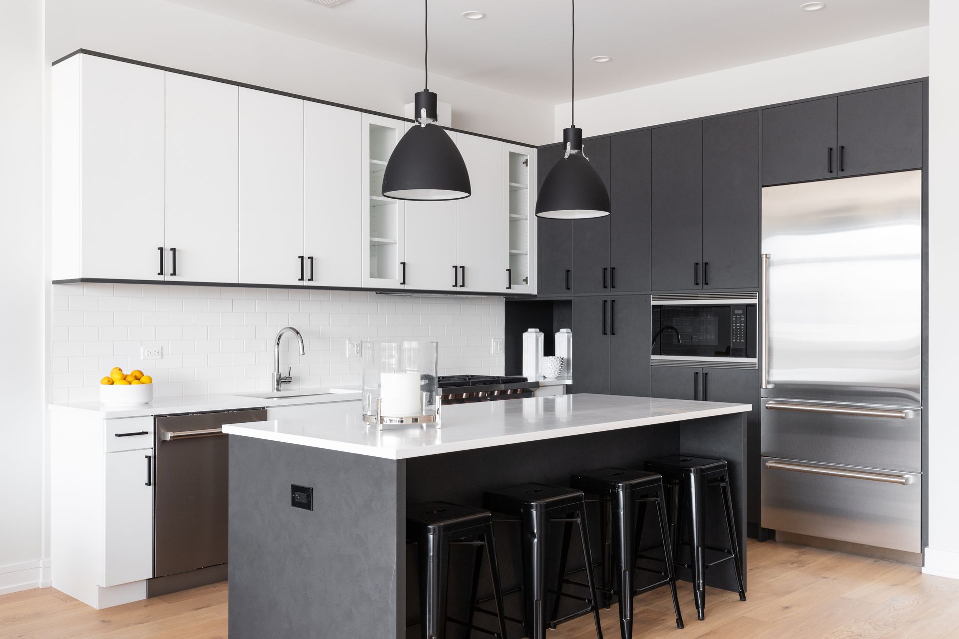 Modern kitchen with black-and-white cabinets, island, pendant lights, and stainless steel refrigerator