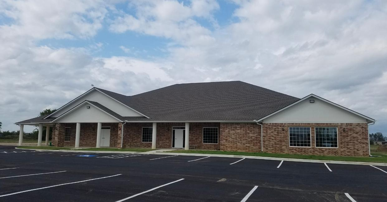 Single-story brick building with a covered entrance and empty parking lot under a cloudy sky