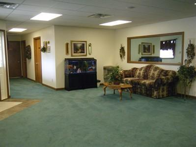 Empty lobby with green carpet, floral couch, coffee table, and framed wall art.