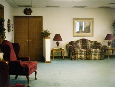 Quiet lobby with green carpet, sofas, armchair, tables, lamps, and a framed picture on the wall.