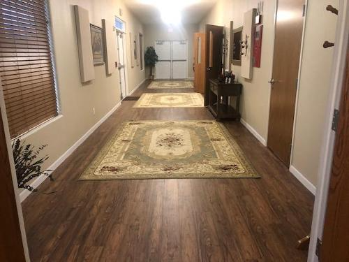 Long beige hallway with wood floors, patterned rugs, framed art, and a bright light at the far end