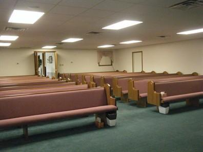 Empty church sanctuary with rows of wooden pews and a green carpet floor