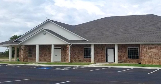 Single-story brick building with a gabled roof and parking lot in front