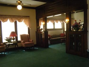 Cozy living room with green carpet, pink armchairs, lamps, and curtained windows
