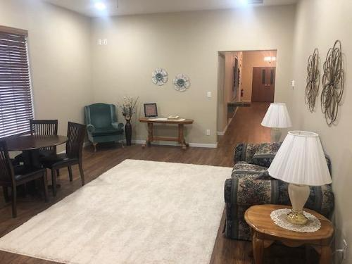 Living room with beige rug, green armchair, sofa, table lamps, and dining area in back