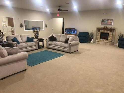 Spacious living room with beige sofas, blue rug, fireplace, ceiling fan, and wall art.