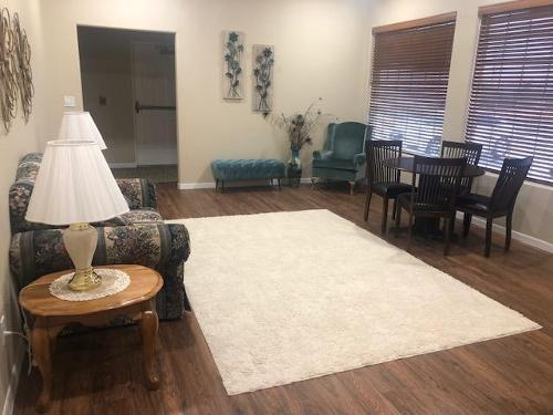 Living room with white rug, sofa, chairs, side table, and blinds on hardwood floor.