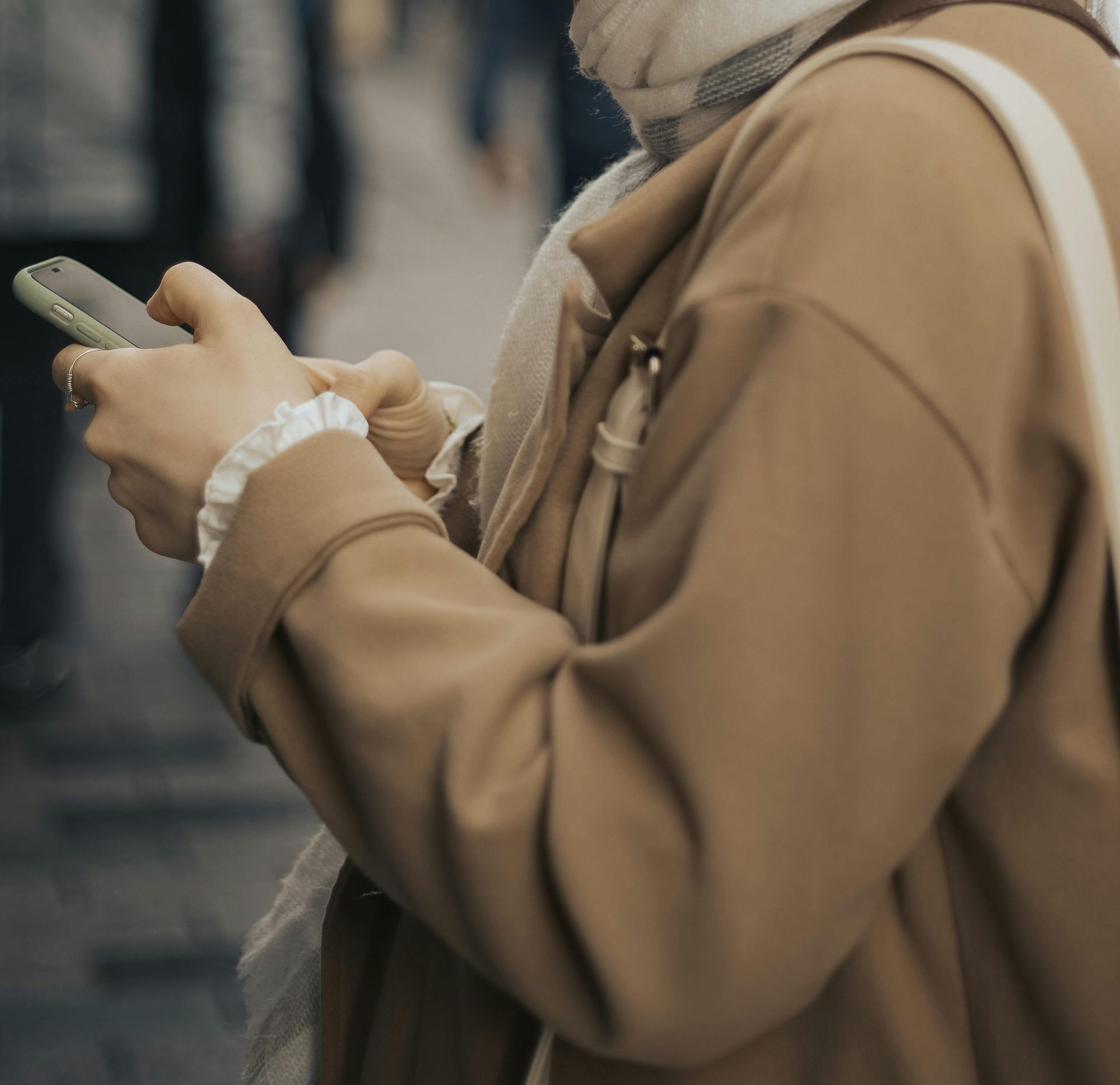 Person in a tan coat using a smartphone outdoors