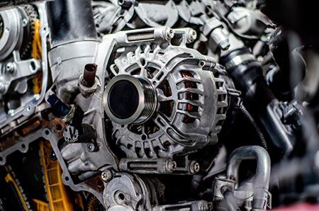 Close-up of a silver car alternator on an engine, with black and gray components.