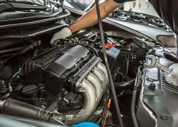 A man is working on the engine of a car with a wrench.