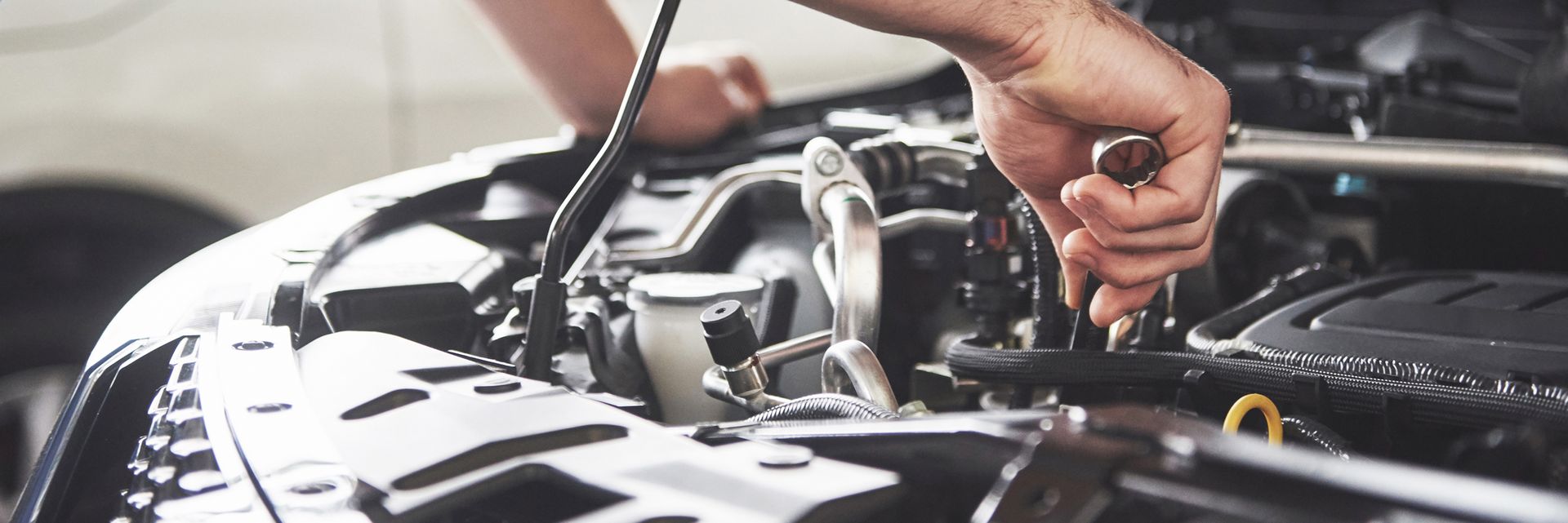 A man is working on the engine of a car with a wrench.