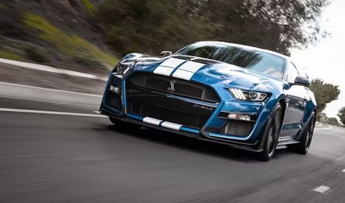 Blue Ford Mustang Shelby GT500 with white racing stripes on a curved road.