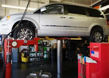 A silver minivan is raised on a car lift in an auto repair shop.