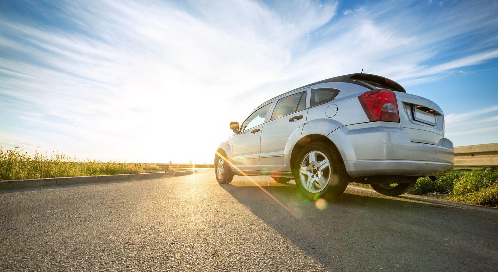 A white car is parked on the side of a road at sunset.