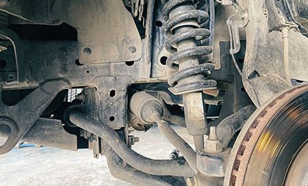 Close-up of a vehicle's suspension system with a shock absorber, coil spring, and brake rotor visible.