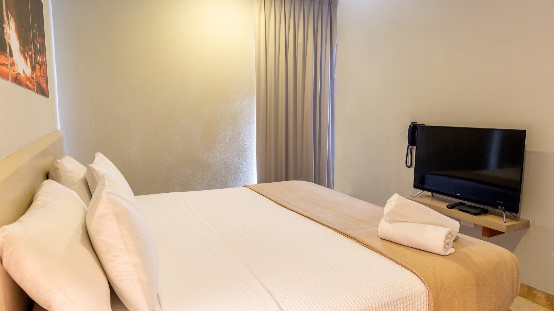 Habitación de hotel bien arreglada con una cama grande, televisión y toallas dobladas a los pies de la cama.