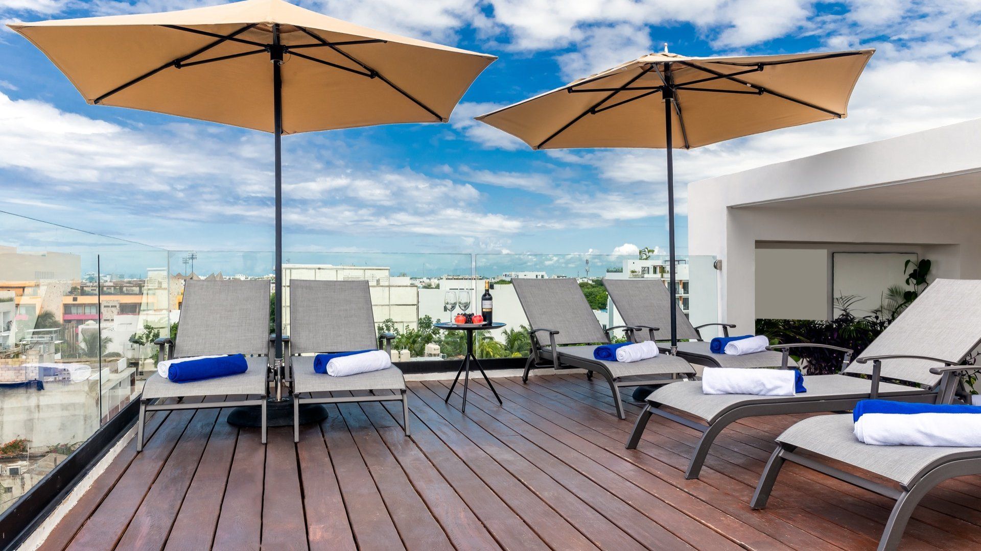 Terraza en la azotea con tumbonas, sombrillas color canela y vistas a la ciudad bajo un cielo azul brillante.