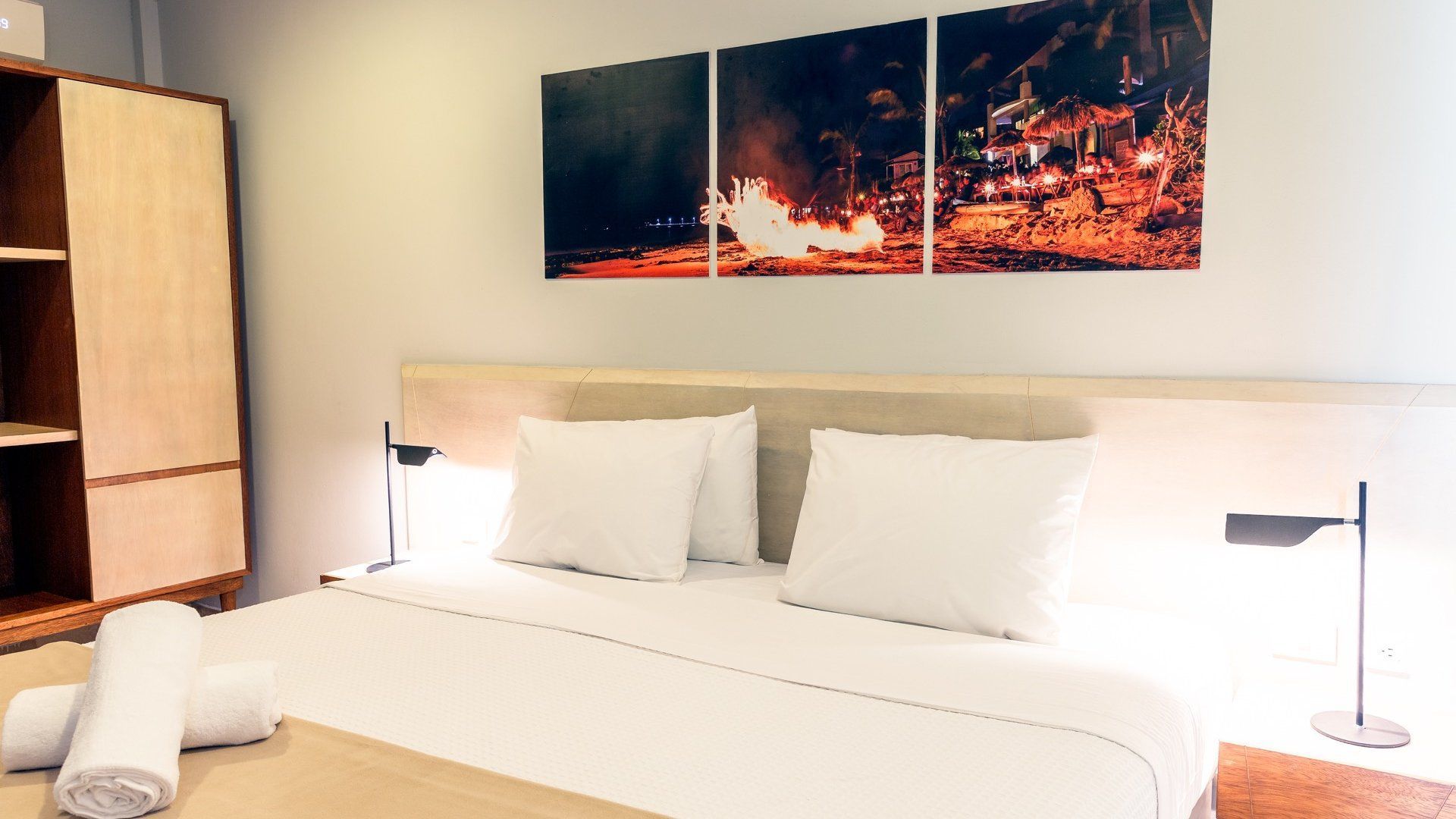 Dormitorio moderno con cama blanca, lámpara de noche y una obra de arte con un paisaje urbano vibrante sobre el cabecero.