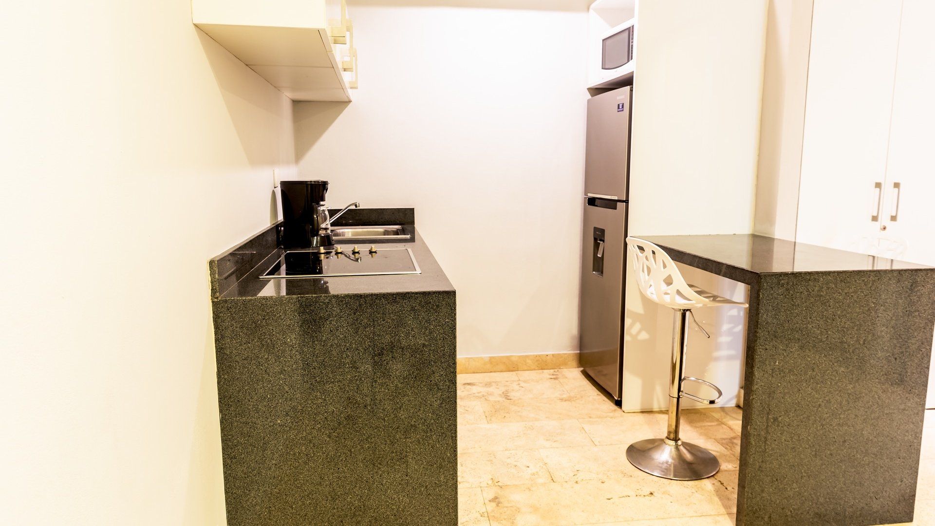 Cocina moderna con encimeras de granito, fregadero negro, nevera de acero inoxidable y taburete blanco.