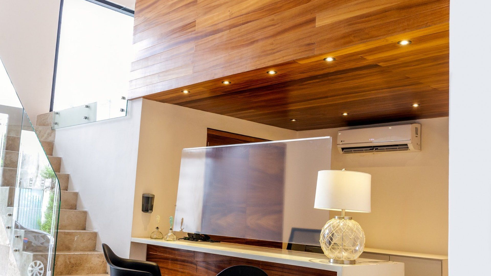 Sala de estar moderna con techo revestido de madera, escalera, lámpara y gran cuadro en la pared.