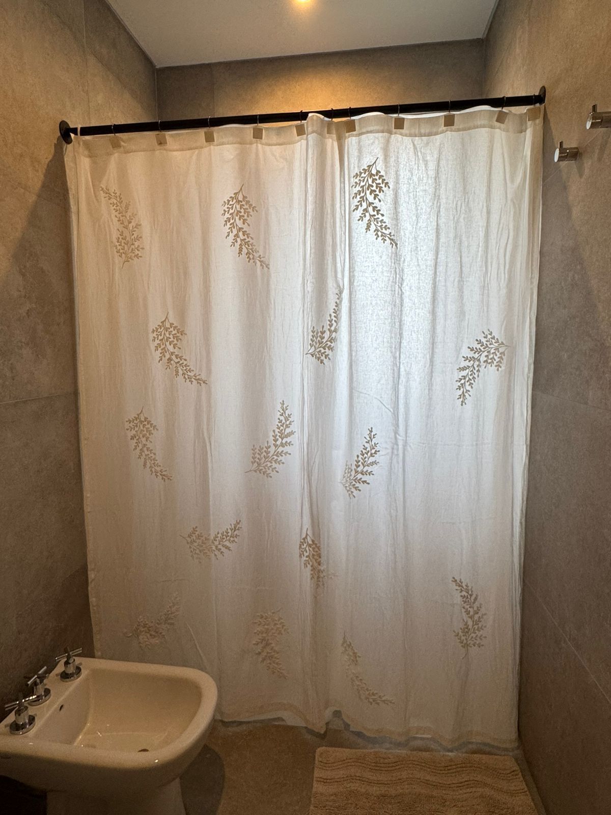 Baño con inodoro blanco, bidé y cortina de ducha con estampado floral. También se aprecian