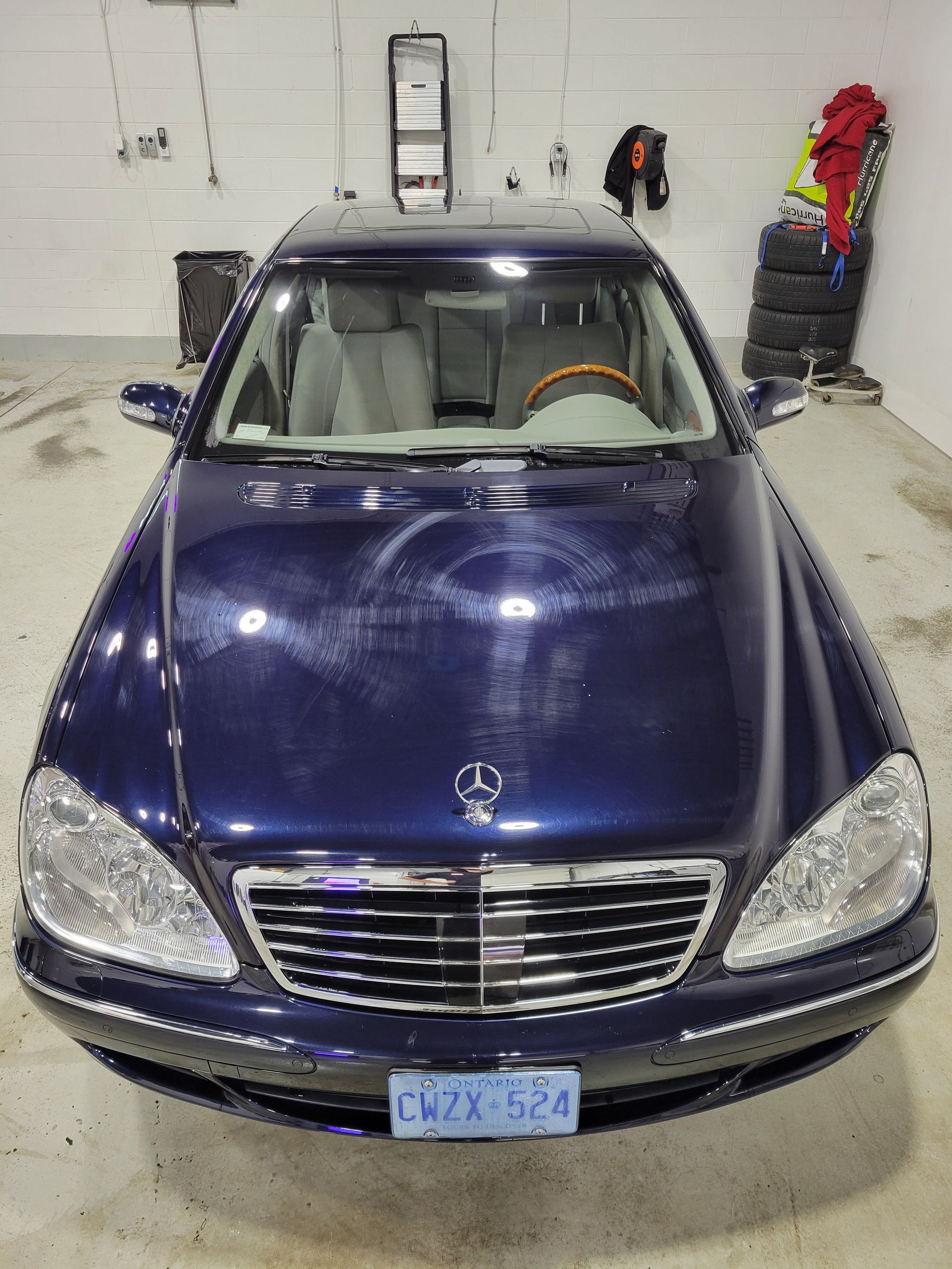 Front view of a blue Mercedes-Benz sedan in a showroom, with light reflections on the hood.