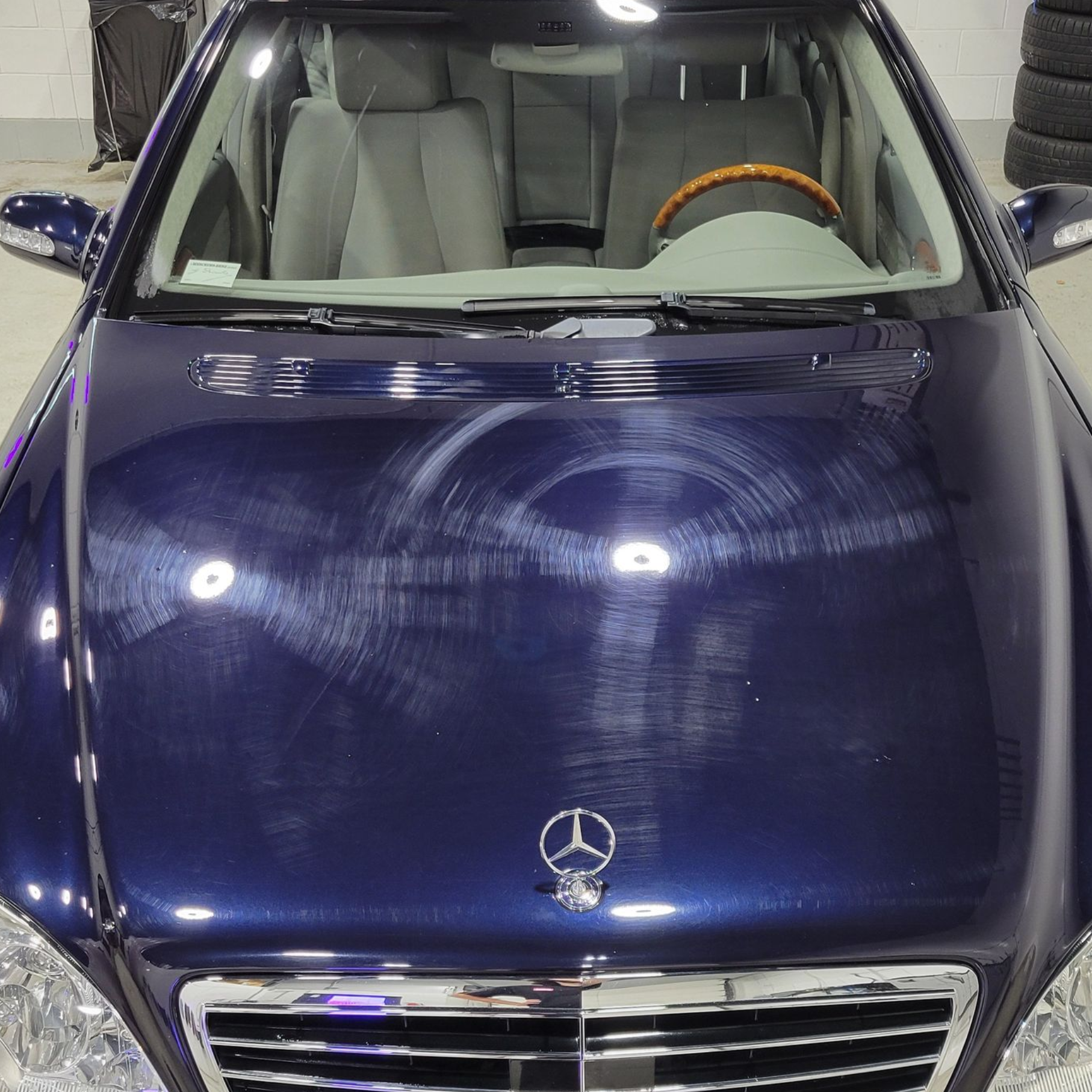 Front view of a dark blue Mercedes sedan in a garage, with wall-mounted car accessories behind it