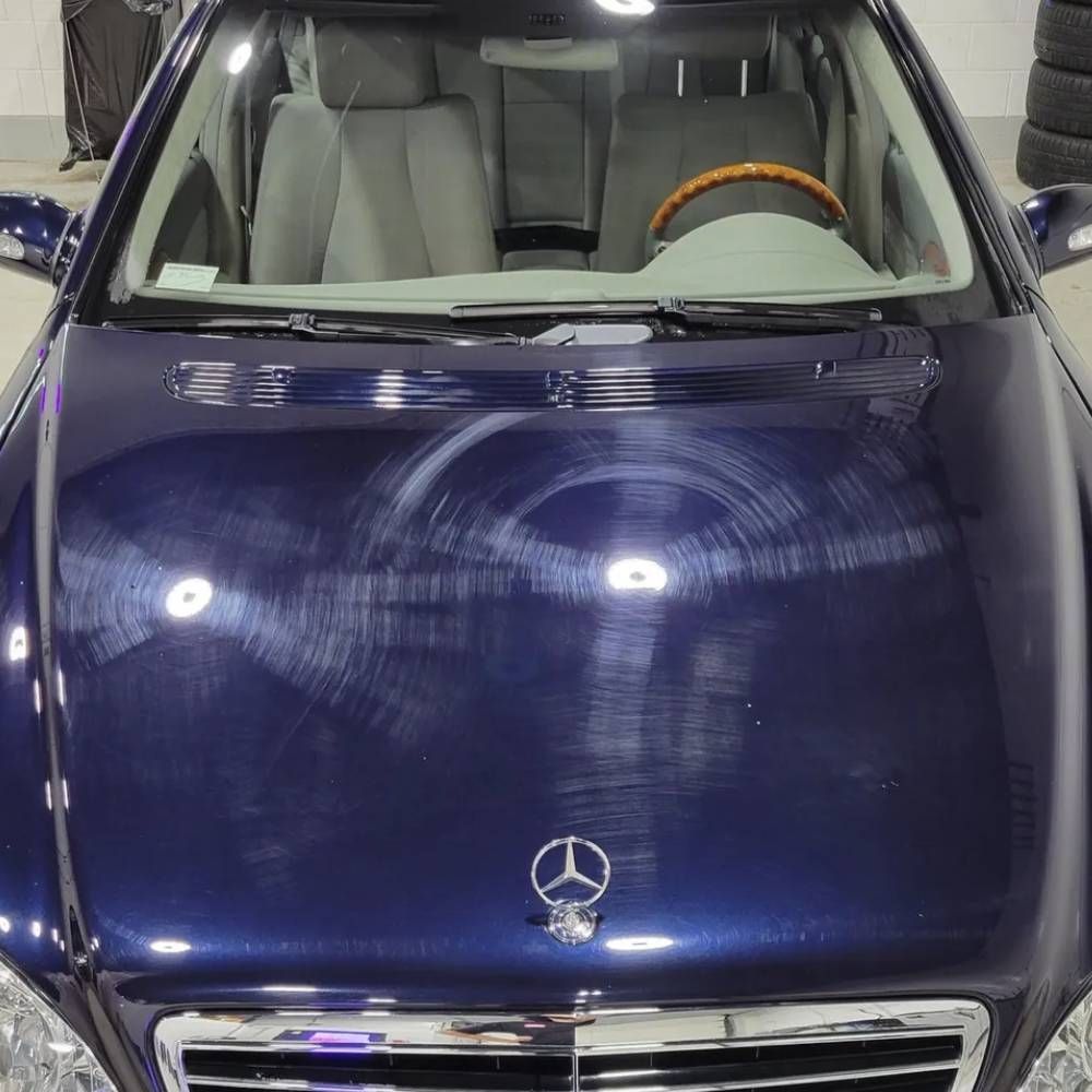 Blue Mercedes car hood with visible swirl marks and reflections, viewed from the front inside a garage