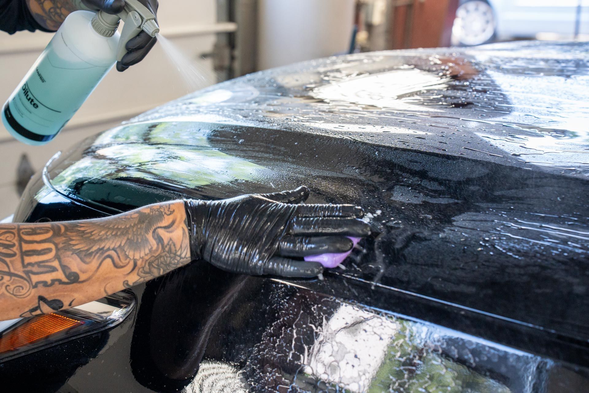 Gloved hand polishing a wet black car roof with spray bottle nearby