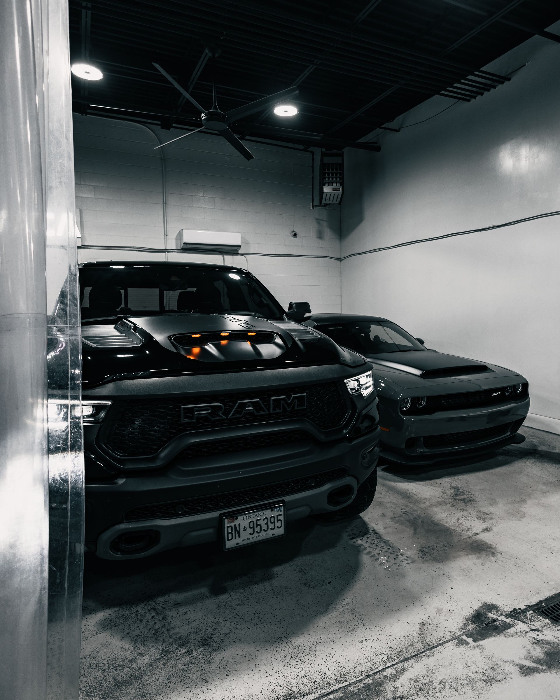 Two black SUVs parked inside a dimly lit garage with concrete walls and ceiling lights