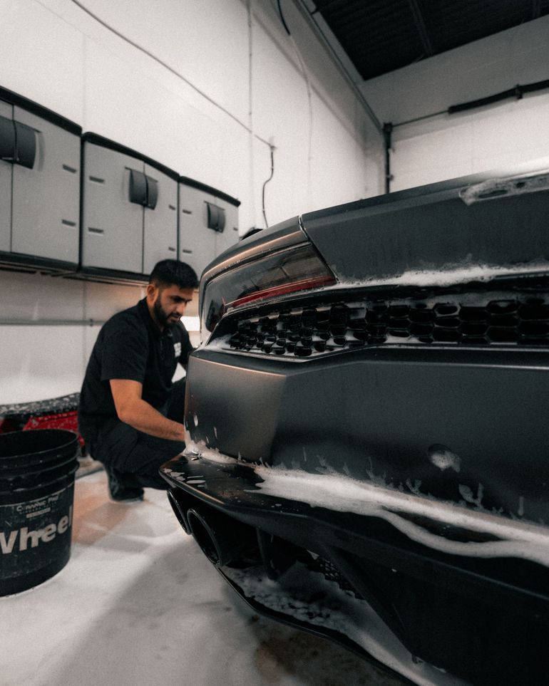 Mechanic working on a black sports car in a garage, close-up on the rear bumper.