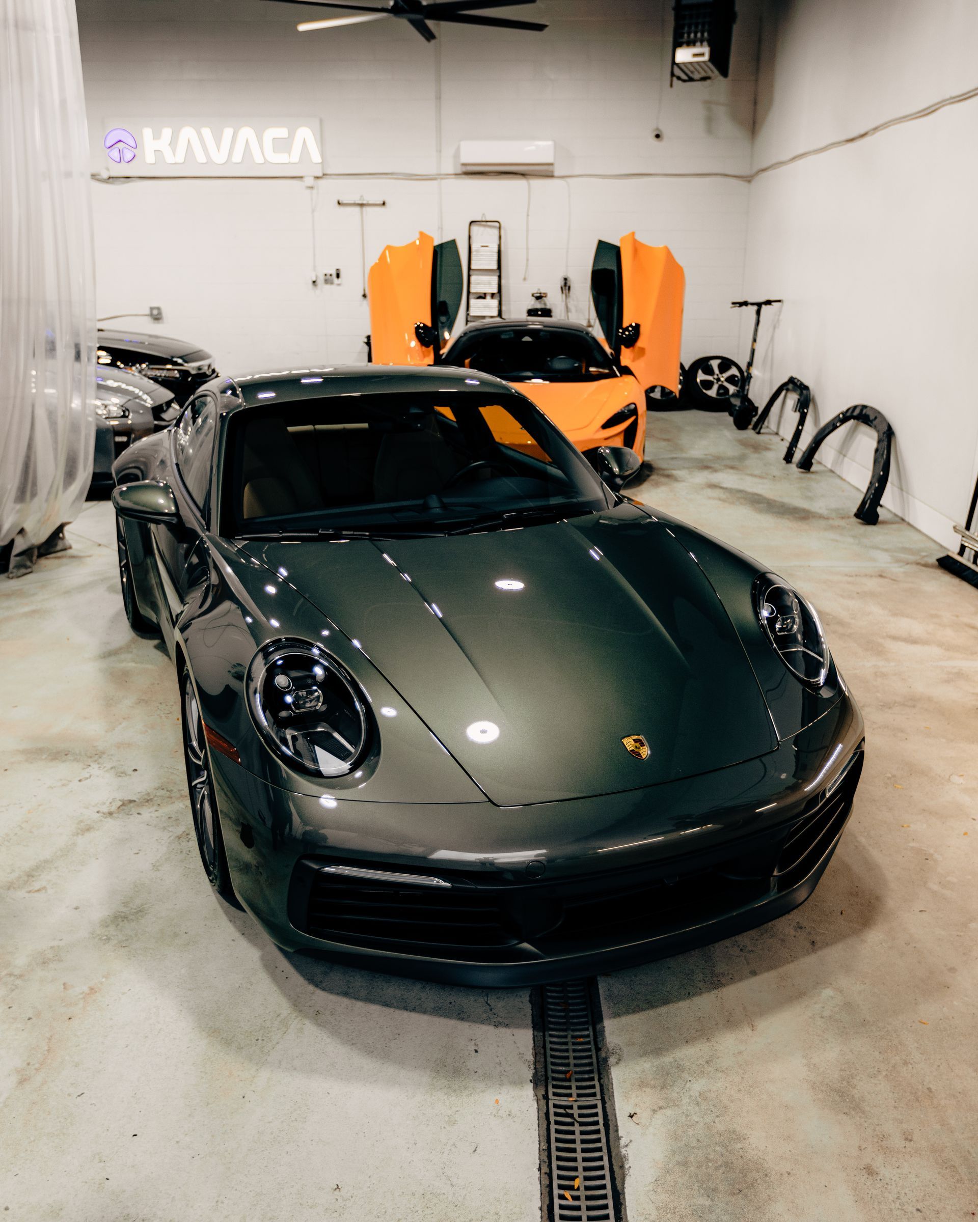 Dark green Porsche in a garage, with orange scissor doors open and a neon sign on the wall.