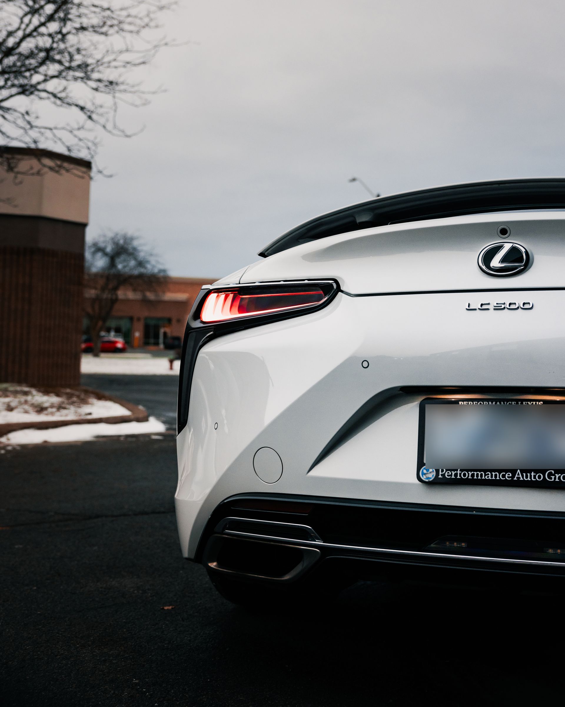 White Lexus sedan parked on a wet street, rear view with taillight and snowy curbside background