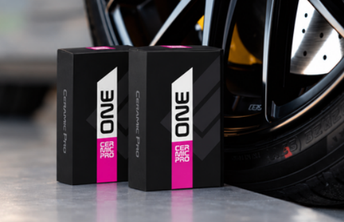 Black alloy wheel with yellow brake caliper beside two black-and-pink ONE product boxes