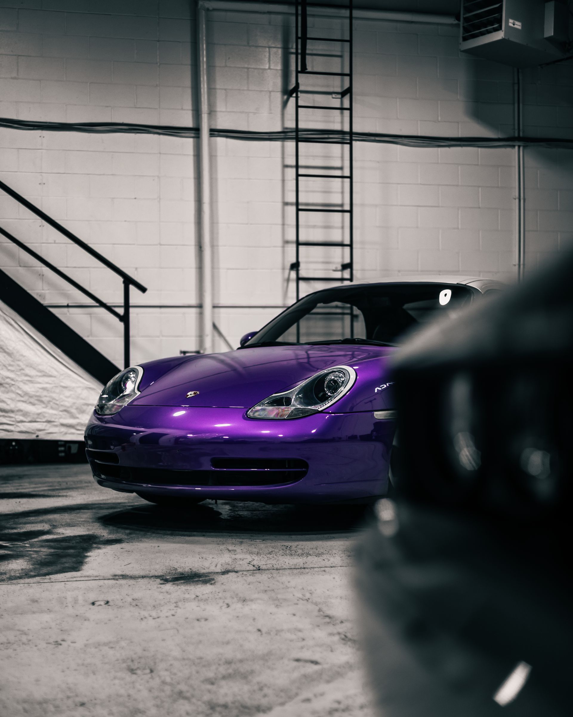 Purple sports car parked in a garage, with a black car blurred in the foreground.