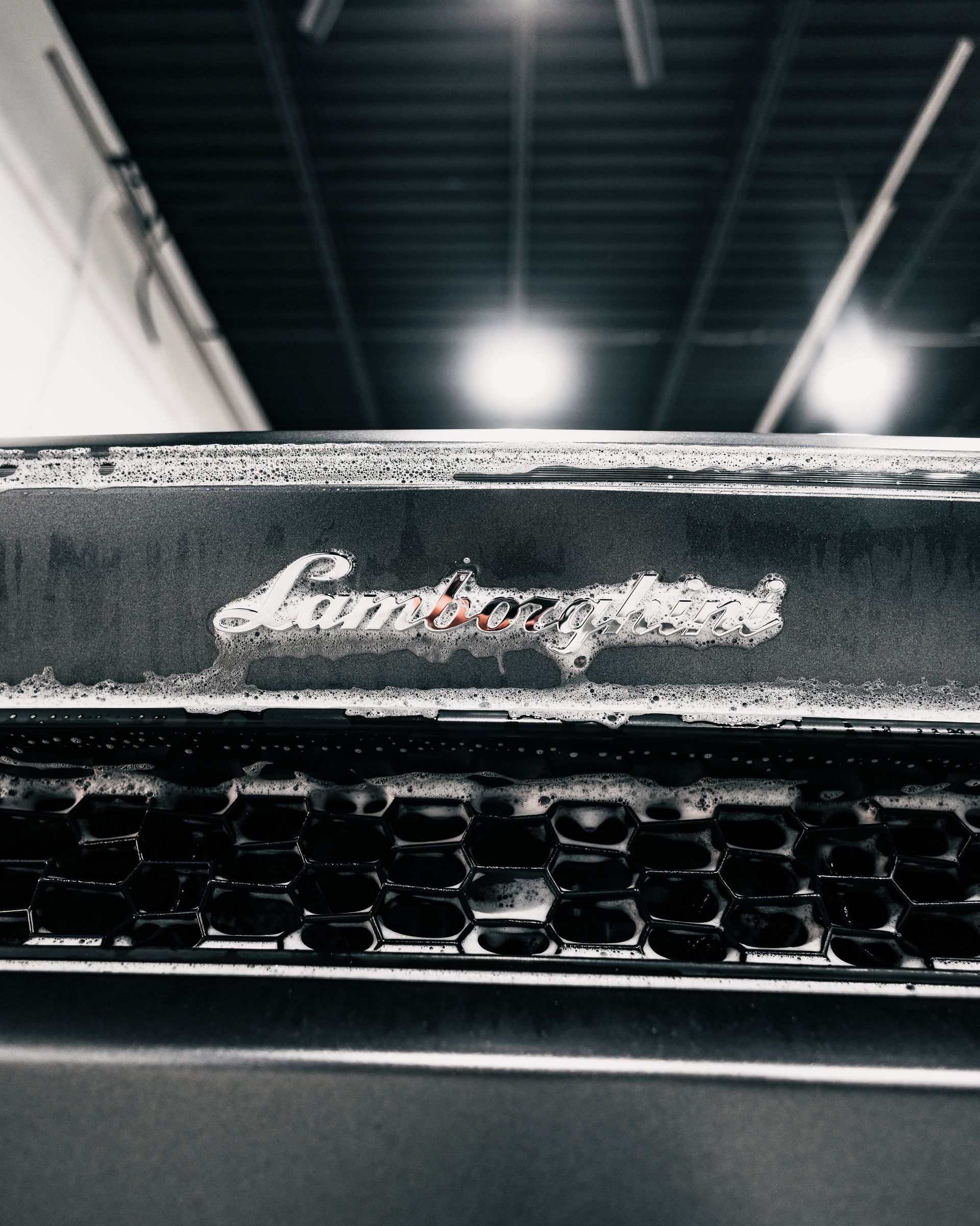 Close-up of a black Lamborghini grille with a blurred industrial ceiling in the background