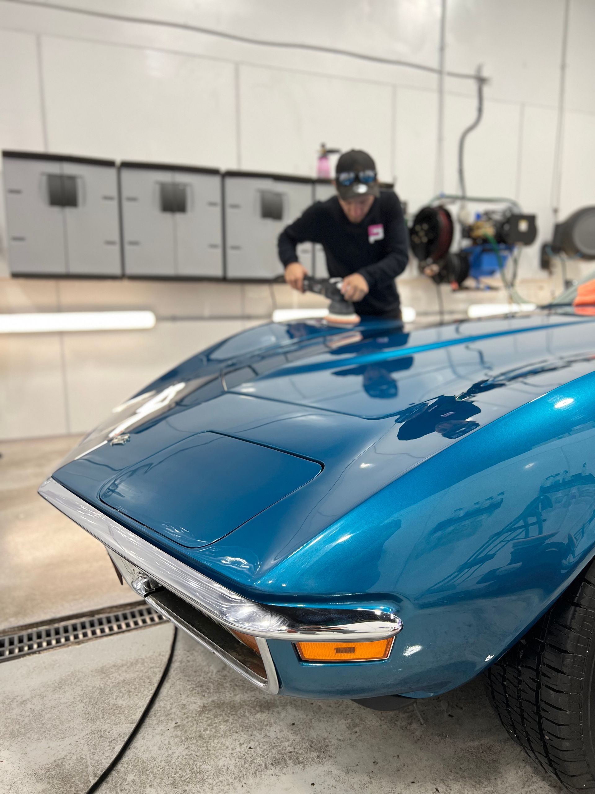 Mechanic polishing a blue sports car in a garage