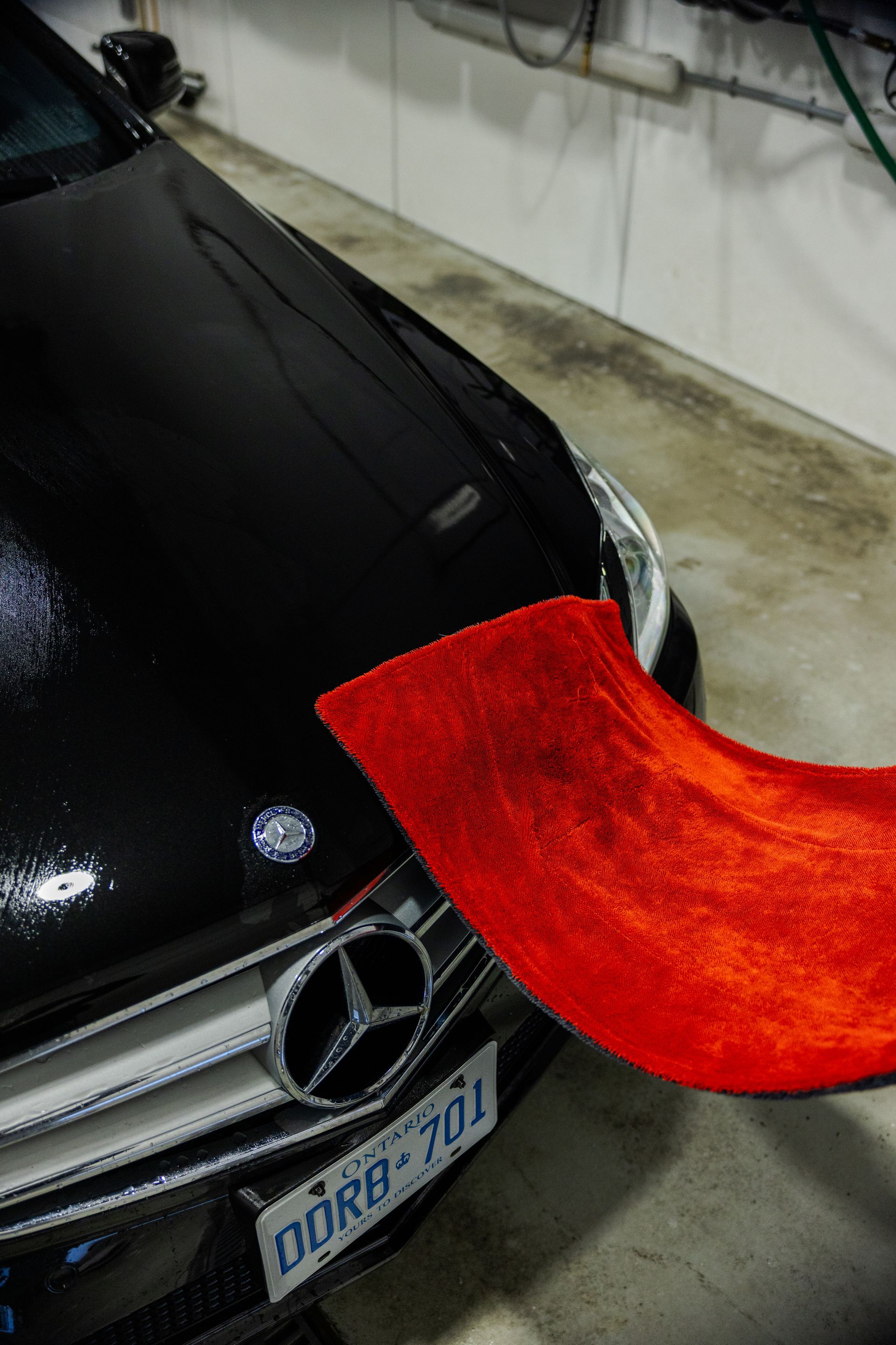 Black Mercedes in a garage with a bright red cloth draped over the front hood and bumper.