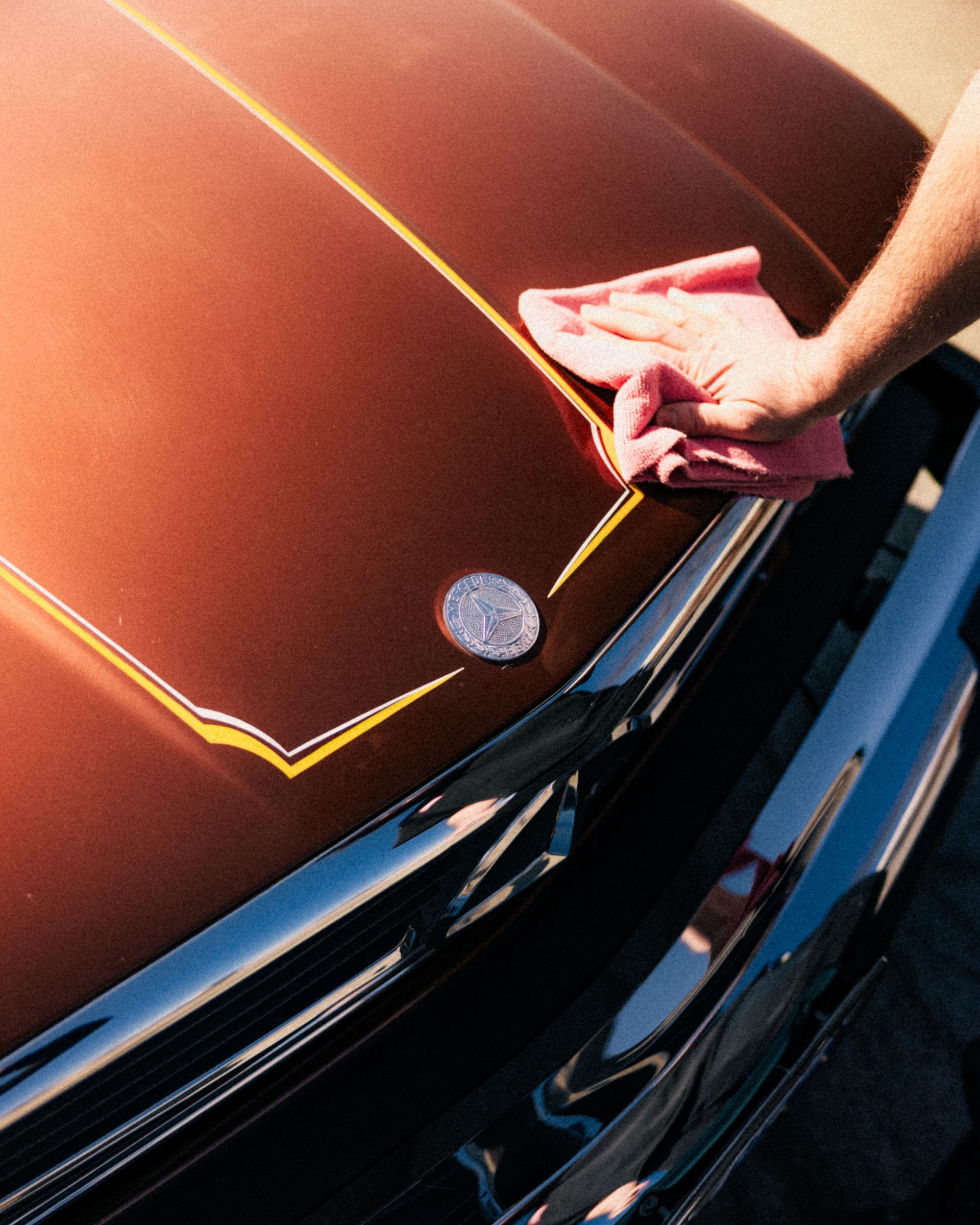 Hand polishing a red car hood with a cloth near the windshield