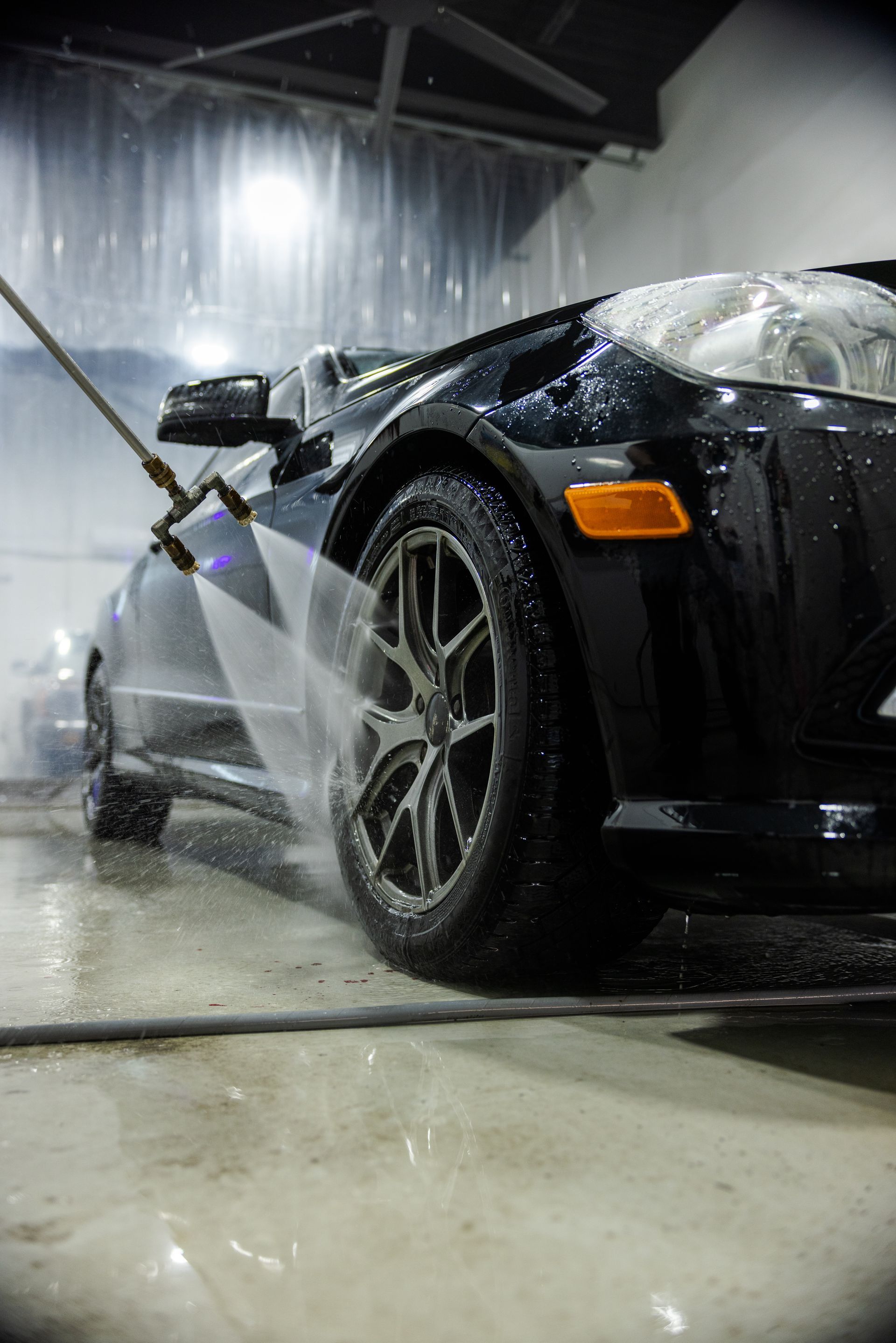 Black sports car being washed with a pressure spray in an indoor car wash