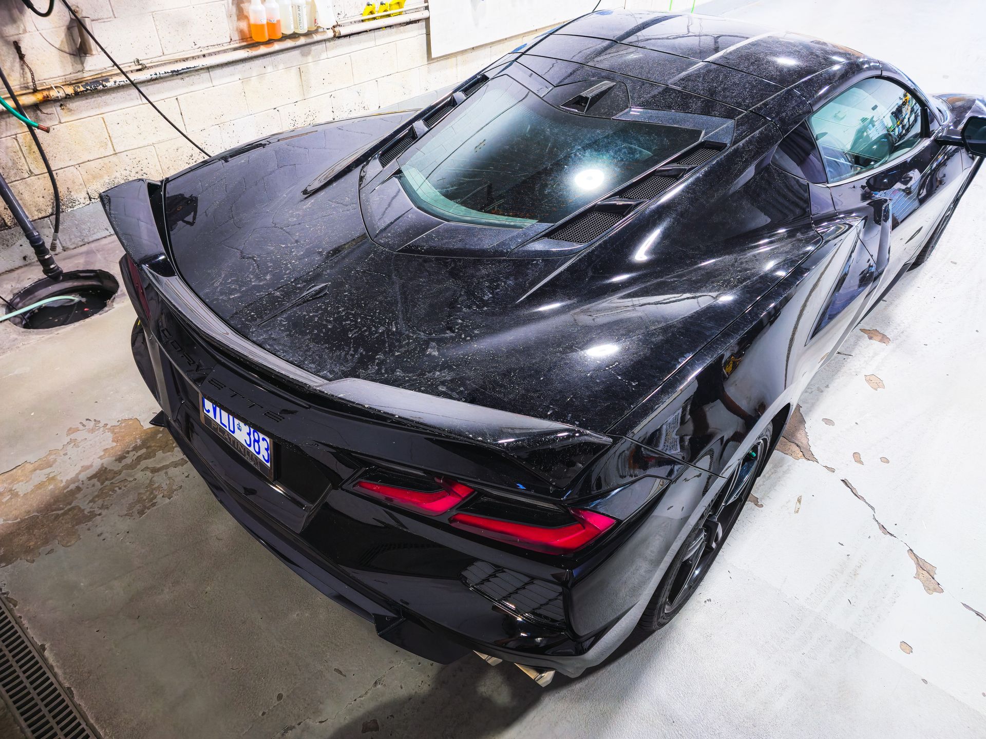 Black sports car parked indoors in a garage, viewed from the rear-left angle.