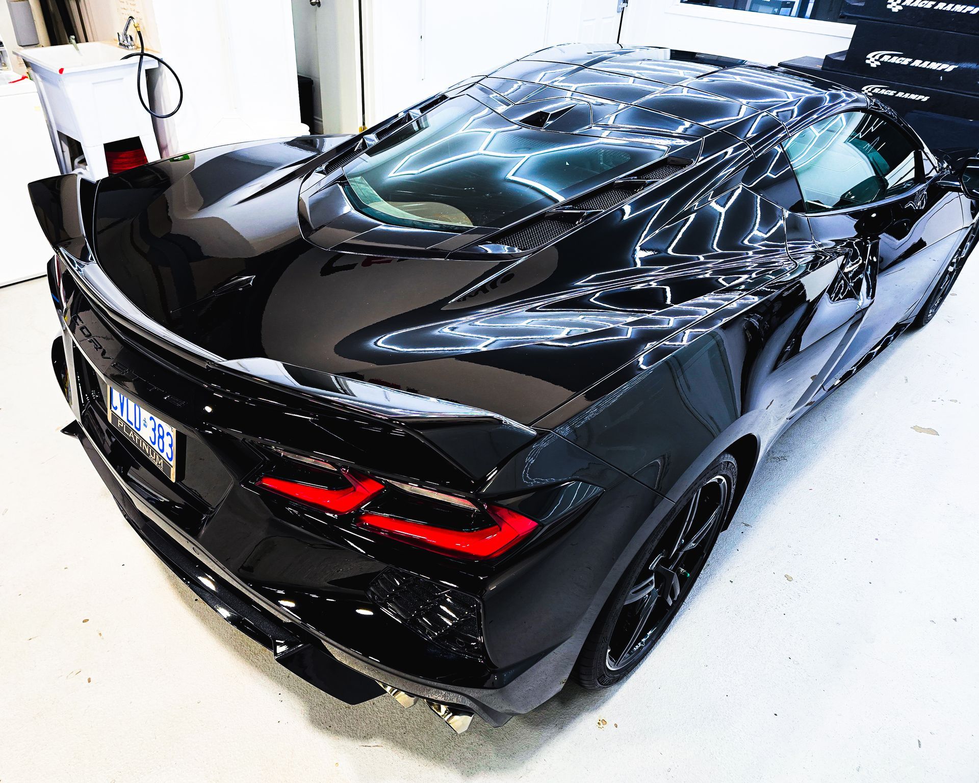 Black sports car parked in a bright garage, rear three-quarter view with red taillights visible