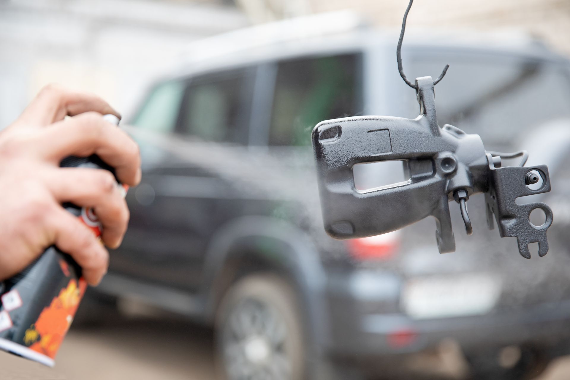 Hand holding a car key fob with a blurred black SUV in the background