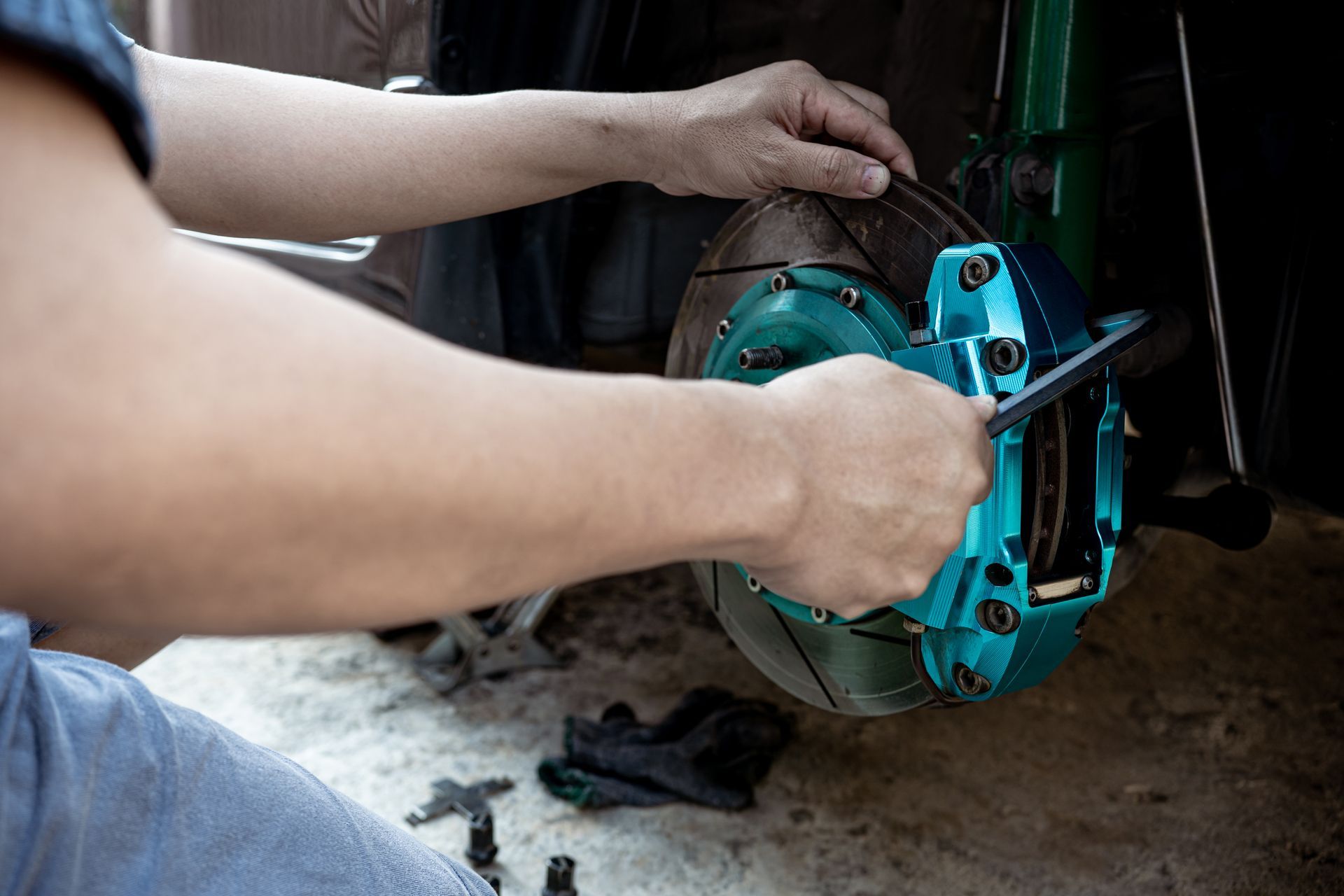 Hands working on a teal car brake assembly under the vehicle