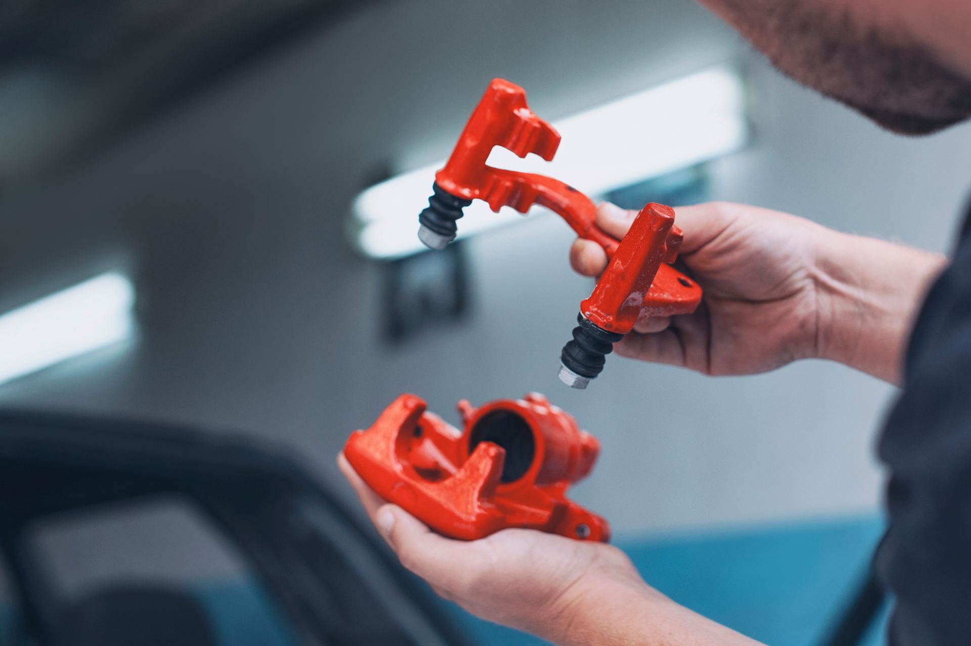 Hands holding red 3D-printed mechanical parts in a workshop
