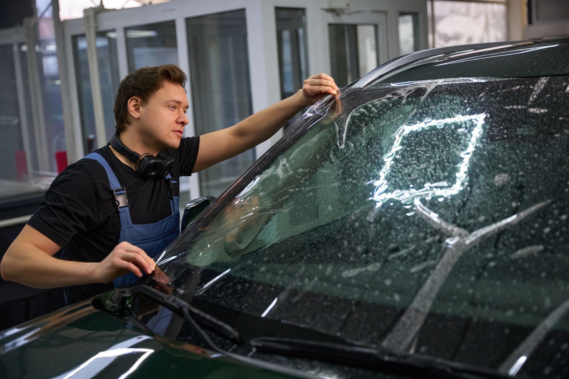 Technician cleaning a car windshield with a squeegee in a garage